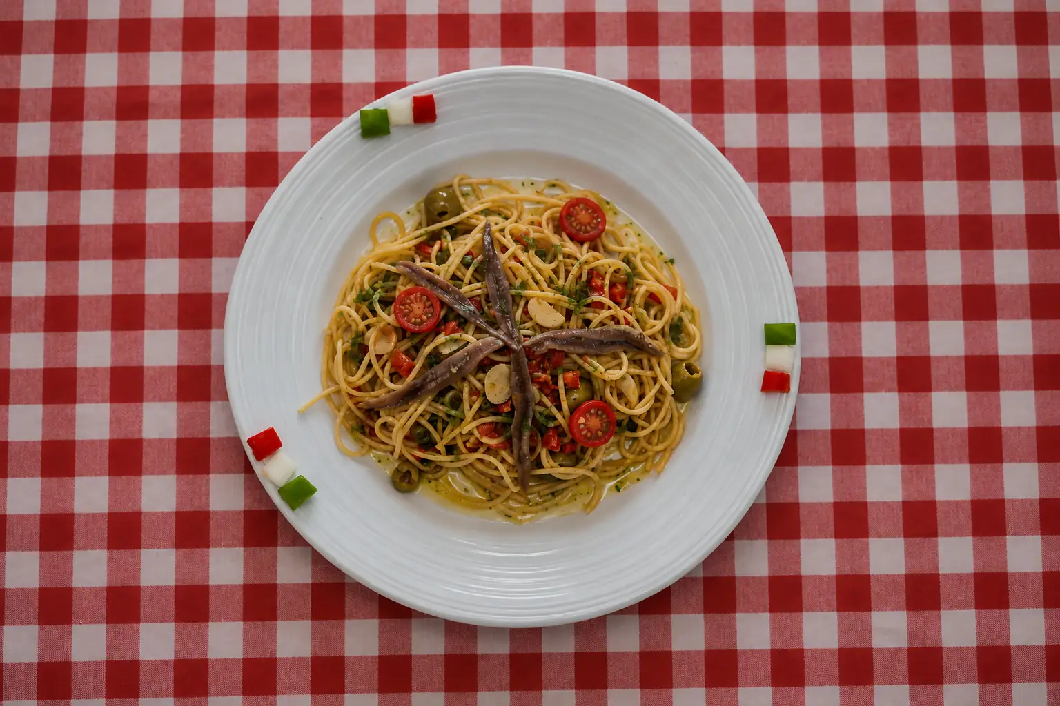 Spaghetti with anchovies, cherry tomatoes and olives on a red-checked tablecloth